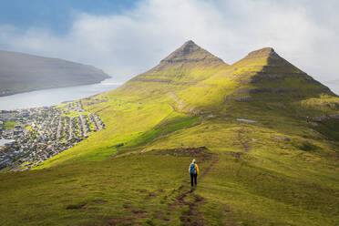 Wanderer mit gelber Jacke geht den Berg Klakker hinunter, Klaksvik, Insel Borooy, Färöer Inseln, Dänemark, Europa - RHPLF23300