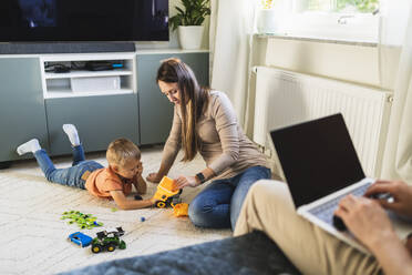 Mutter und Sohn spielen mit Spielzeug, während der Vater zu Hause auf dem Sofa arbeitet - DMMF00183