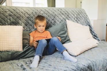 Cute boy with tablet PC sitting on sofa at home - DMMF00185