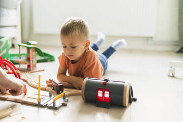 Son lying on floor and looking at toy train at home - DMMF00190