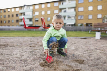 Cute boy splashing sand with shovel in playground - DMMF00202