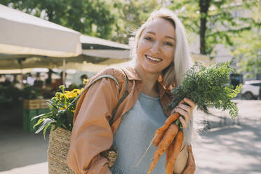 Lächelnde Frau mit Korbtasche und Karotten auf dem Markt - NDEF00004