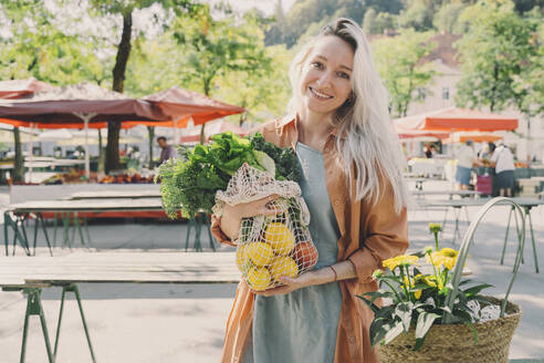 Smiling woman with fresh vegetables in mesh bag at market - NDEF00010