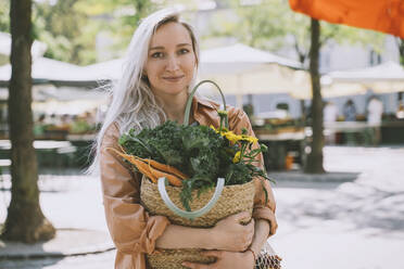 Kundin mit Bio-Gemüse und Blumen in einer Korbtasche auf dem Markt - NDEF00013