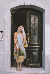 Smiling woman with grocery bag standing near doorway - NDEF00027