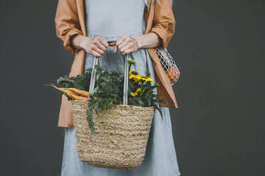 Frau hält kostenlose Plastiktüte mit Gemüse und Blumen vor grauem Hintergrund - NDEF00030