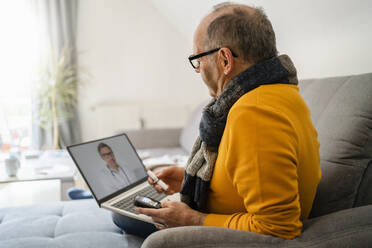 Man doing online consultation with doctor through laptop on sofa at home - DIGF19022