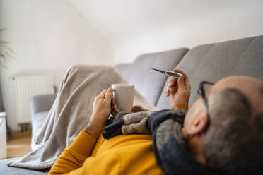 Mann misst Fieber mit einem Thermometer auf dem Sofa zu Hause - DIGF19024