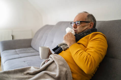 Man coughing sitting on sofa in living room - DIGF19027