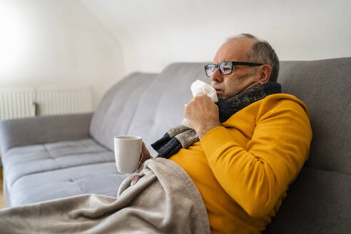 Mann hustend auf Sofa im Wohnzimmer sitzend - DIGF19027