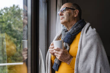 Nachdenklicher Mann mit Tee und Blick aus dem Fenster zu Hause - DIGF19032