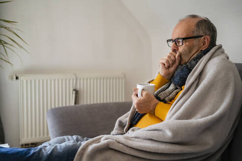Mann mit Becher und Kältegefühl auf dem Sofa zu Hause - DIGF19036