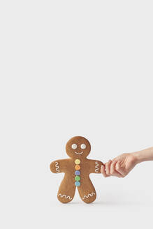 Hand of woman holding freshly backed gingerbread cookie against white background - YDF00002