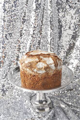 Frisch gebackener Panettone-Kuchen auf einem Kuchenständer vor glänzenden silbernen Pailletten - YDF00028