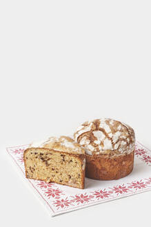 Ganzer und in Scheiben geschnittener Panettone-Kuchen auf gestickter Serviette vor weißem Hintergrund - YDF00034