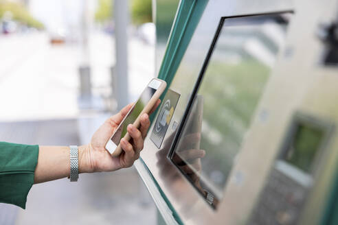 Hand einer Frau, die mit einem Smartphone einen Fahrkartenautomaten scannt - WPEF06532