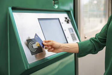 Eine Frau tippt mit der Hand auf eine Kreditkarte am Fahrkartenautomaten einer Straßenbahnhaltestelle - WPEF06534