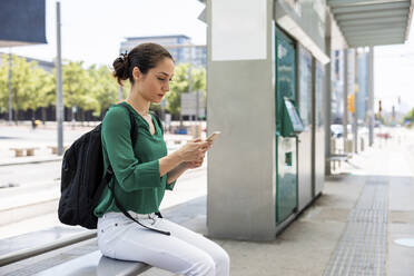 Frau mit Rucksack und Smartphone an der Straßenbahnhaltestelle - WPEF06536