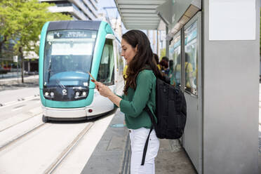 Frau benutzt Smartphone an der Straßenbahnhaltestelle - WPEF06538