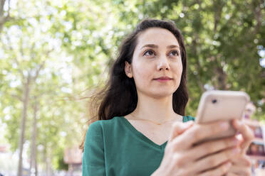 Woman with smart phone standing in front of trees - WPEF06553