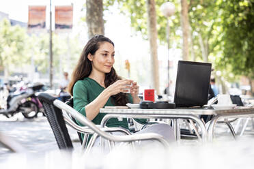 Smiling woman using laptop at sidewalk cafe - WPEF06557