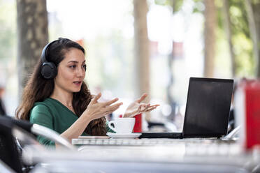 Geschäftsfrau bei Videogespräch über Laptop in einem Straßencafé - WPEF06561