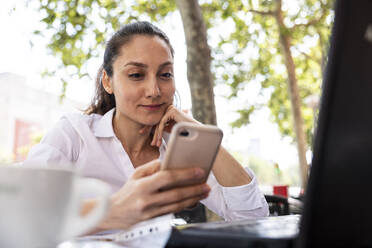 Lächelnder Freiberufler, der in einem Straßencafé sein Mobiltelefon benutzt - WPEF06570