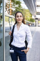 Smiling businesswoman with hand in pocket standing at footpath - WPEF06577