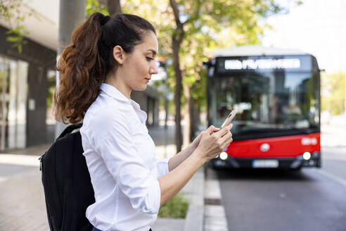 Geschäftsfrau mit Smartphone vor einem Bus stehend - WPEF06584