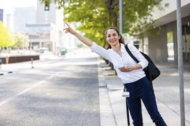 Happy businesswoman hailing for ride standing at footpath - WPEF06588