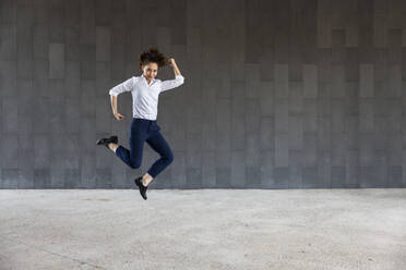 Carefree woman jumping in front of wall - WPEF06590