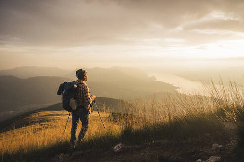 Mature man with hiking pole and backpack looking at sunrise - UUF27585
