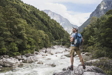 Älterer Mann mit Rucksack steht auf einem Felsen am Fluss - UUF27598