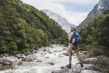 Mature man with backpack standing on rock by river - UUF27598