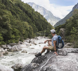 Mature man with backpack sitting on rock by river - UUF27601