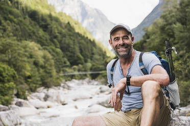Happy mature man sitting in front of mountains - UUF27602