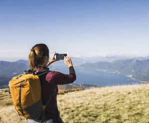 Frau fotografiert mit Smartphone an einem sonnigen Tag - UUF27622