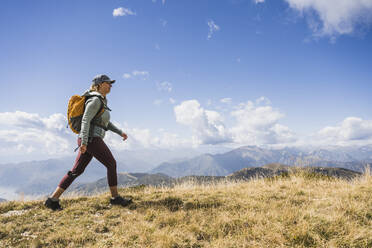 Mature woman walking on grass under cloudy sky - UUF27646