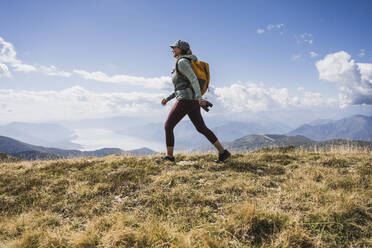 Woman walking on grass in front of cloudy sky - UUF27647