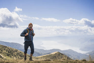 Glücklicher Mann beim Wandern auf einem Berg vor einem bewölkten Himmel - UUF27651