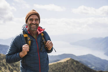 Glücklicher reifer Mann mit Strickmütze an einem sonnigen Tag - UUF27656