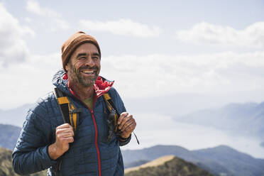 Fröhlicher reifer Mann mit Strickmütze, stehend mit Rucksack - UUF27657