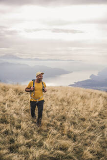 Lächelnder Mann mit Mütze beim Wandern auf einem Berg - UUF27658