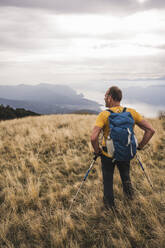 Mature man standing with backpack and hiking poles on grass - UUF27666