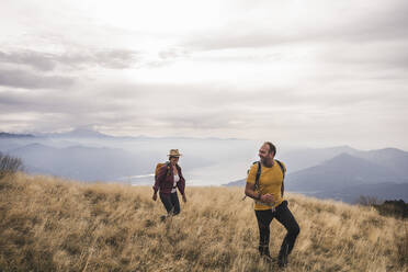 Glückliches reifes Paar beim Wandern auf einem Berg unter bewölktem Himmel - UUF27667