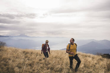 Happy mature couple hiking on mountain under cloudy sky - UUF27667