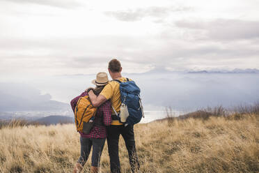 Couple with backpacks standing on grass under cloudy sky - UUF27674