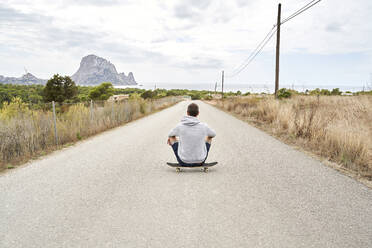 Man sitting on skateboard under cloudy sky - VEGF06013