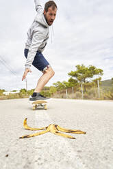 Verängstigter Mann fährt mit dem Skateboard durch eine Bananenschale auf der Straße - VEGF06022