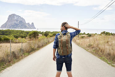 Man wearing backpack standing with hand behind head on road - VEGF06024